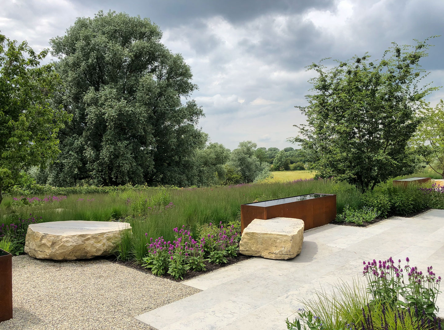 Cambridgeshire Garden design by Colm Joseph modern natural stone terrace and corten steel water feature and boulder seats with wildlife friendly planting and countryside views