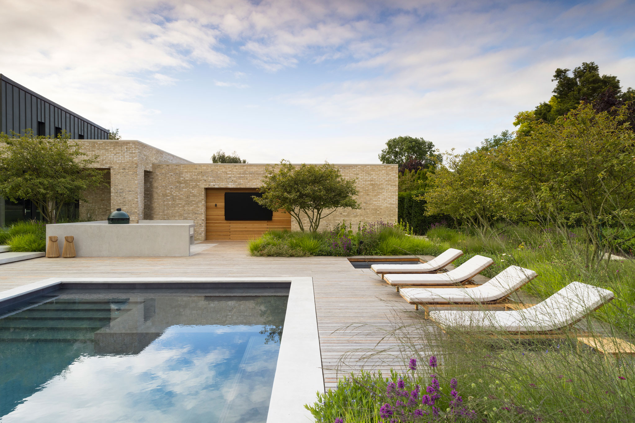 Colm Joseph modern country garden home cambridgeshire swimming pool reflections timber deck sun loungers naturalistic planting design concrete outdoor kitchen amelanchier trees